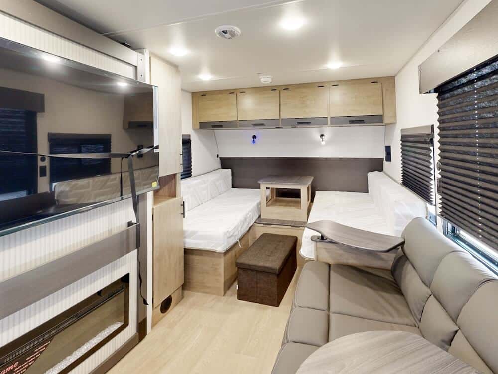 Image of the interior of the Campsite Reserve 20AJ facing the front of the RV. It includes a TV to the left, sofa to the right and covertible dining area straight ahead. 