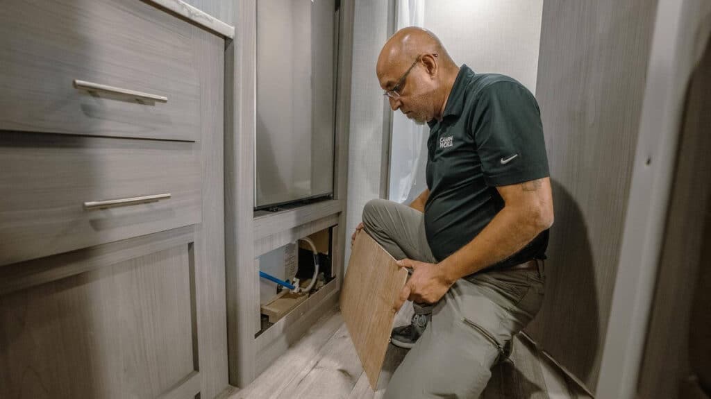 Technician accessing back of RV water heater from inside