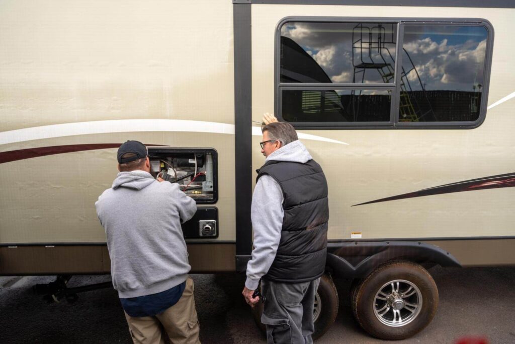 Two technicians testing fridge at exterior access panel