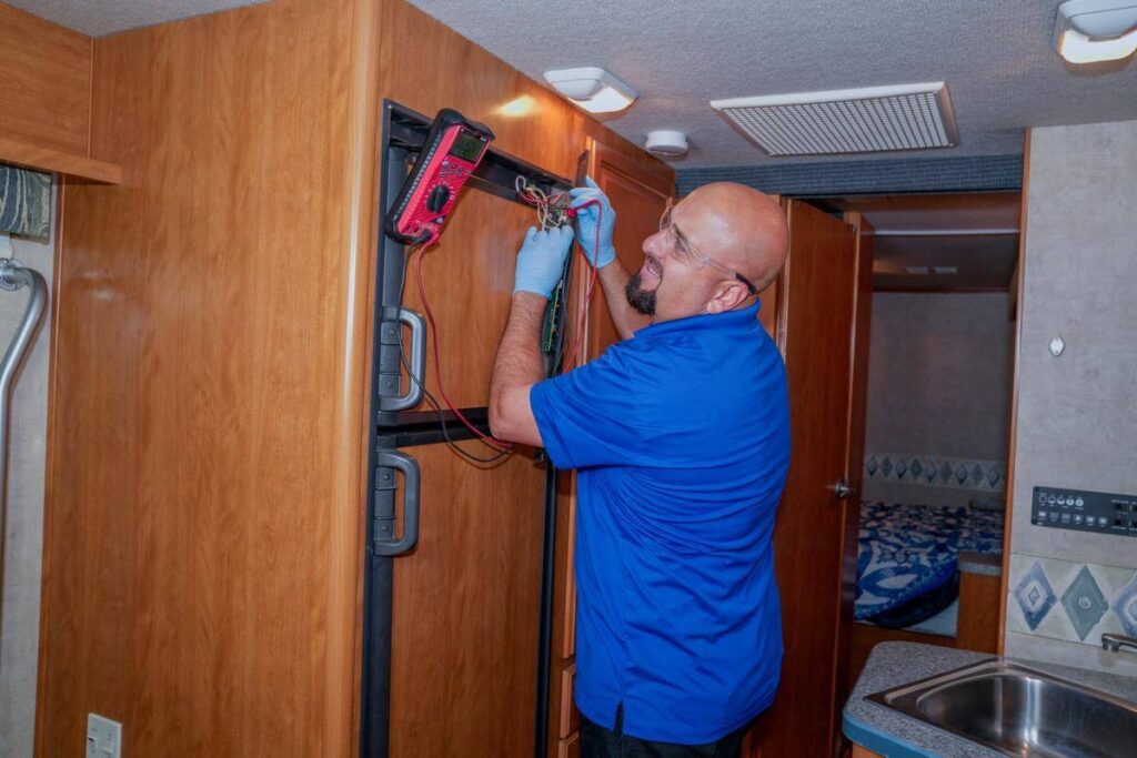 Technician troubleshooting RV refrigerator using a multimeter