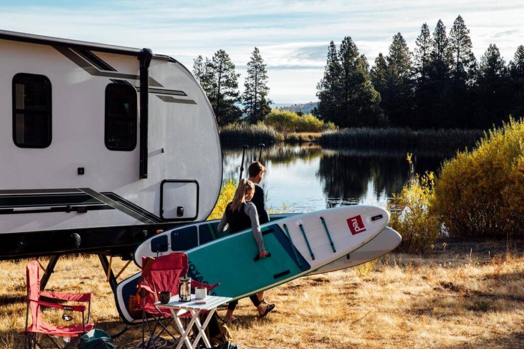 Couple carrying paddleboards for summer camping essentials