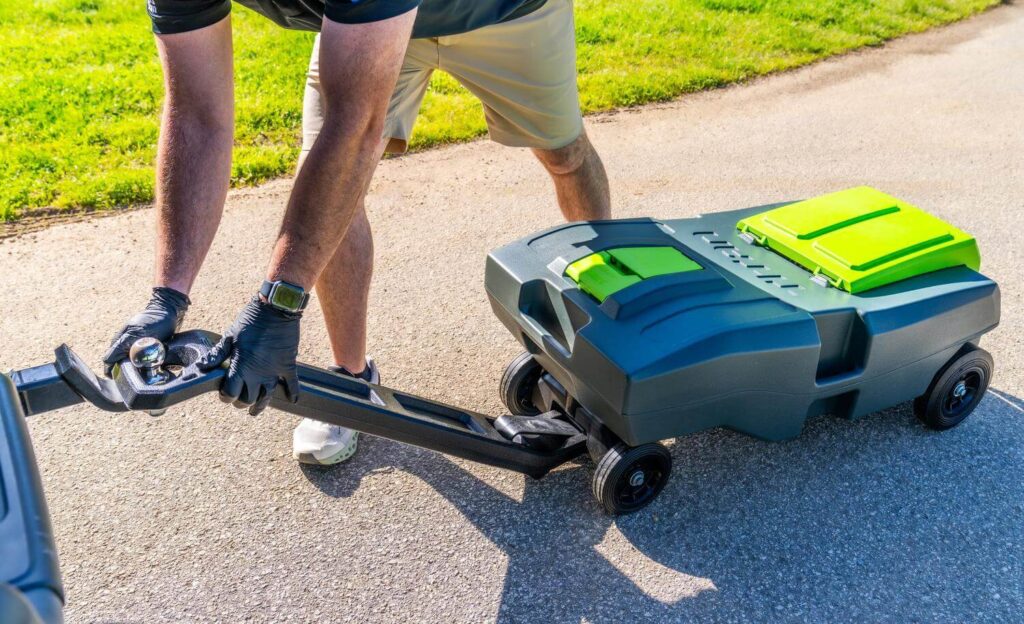 Man attaching portable waste tank for RV to trailer hitch