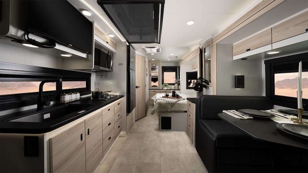 Interior image of the Jayco Melbourne Prestige 25LP Class C RV. It includes a galley kitchen on the left, dinette on the right and faces toward the rear bedroom of the RV.