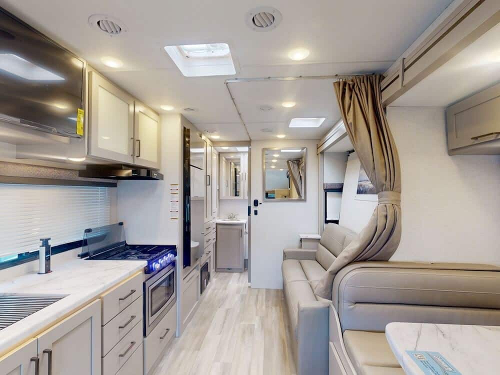 Interior image of the living area for the Thor Coleman 24CL RV. The left of the image features a galley kitchen and the right features part of the dinette and the sofa.