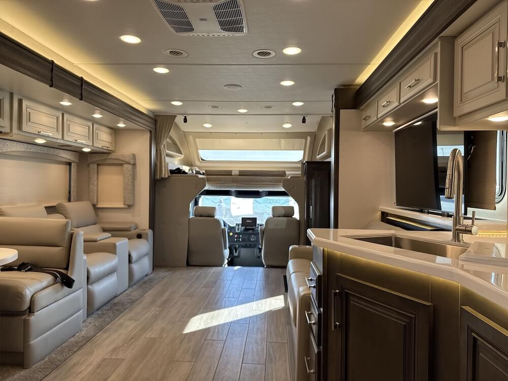 Interior image of the Jayco Seneca Prestige 37M. It faces the cab of the RV and features theater seating to the left and a jackknife sofa and the kitchen sink to the right.