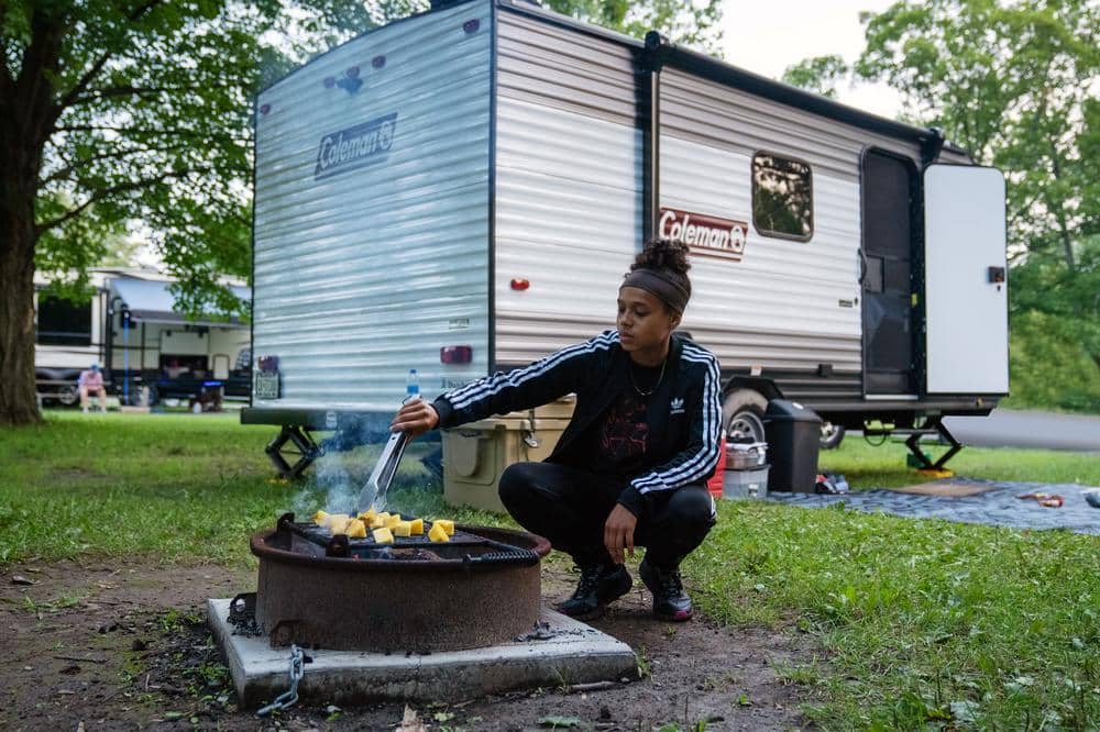 Coleman travel trailer with person lighting fire in front