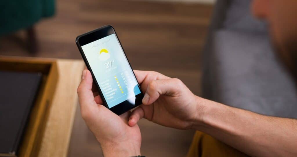 Close up of a young man looking at the daily weather on his smartphone app